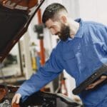 Mechanik w niebieskim kombinezonie sprawdza silnik auta w garażu