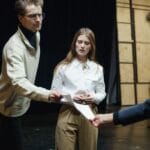 Młodzi aktorzy podczas próby teatralnej z tekstami ról na scenie