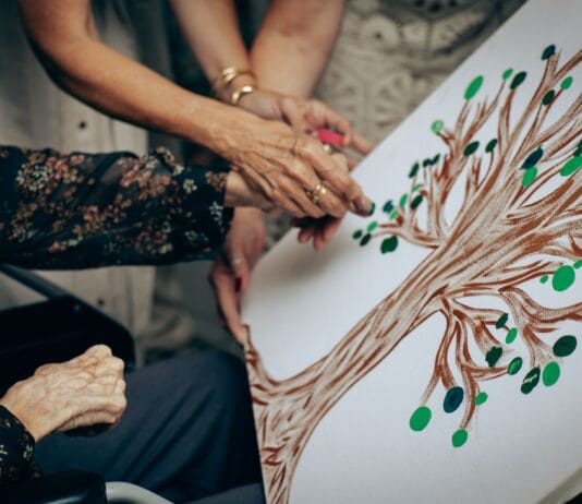 Senior i opiekun malują wspólnie obraz drzewa na płótnie